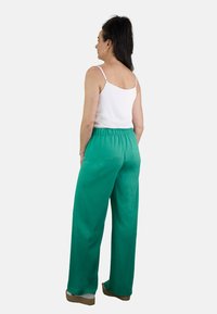 Pantalones anchos verdes hechos de una tela suave con una cinturilla elástica. Combinados con una camiseta blanca de tirantes, mostrando un ajuste relajado y un estilo casual.