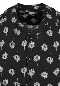 Chemise noire à manches courtes avec motif de feuilles blanches, dotée d'un col classique et de deux boutons. En tissu léger. Taille M.