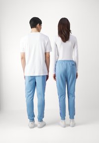 Light blue jogger pants with a drawstring waist, featuring a side stripe pattern. Paired with white t-shirts and white sneakers.