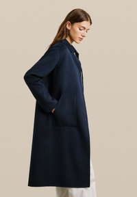 Lange marineblauwe jas van textuurstof, met een kraaghals en zijzakken, ontworpen met een knoopsluiting en een rechte silhouet.