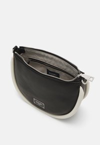 Bolso de cuero negro con forma curva y asas blancas. Presenta un cierre superior de cremallera y un pequeño bolsillo interior. Logo de JOOP! en la parte delantera.