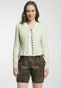 Hellgrüne gerippte Jacke mit Knopfverschluss und Rundhalsausschnitt, kombiniert mit braunen Shorts mit bestickten Details und Knöpfen an den Seiten.