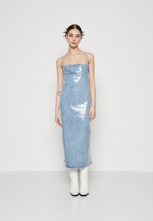 Denim dress with a shiny finish, square neckline, thin straps, and a long form-fitting silhouette. Accented with white knee-high boots.