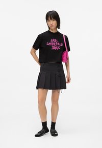 Černé zkrácené tričko s růžovým grafickým textem, v kombinaci s černou plisovanou sukní s bočním šněrováním, černými ponožkami a černými balerínami, spolu s růžovou kabelkou.