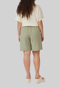 Beige top met korte mouwen gecombineerd met lichte groene shorts, voorzien van een elastische tailleband. Model draagt crème platform sandalen.