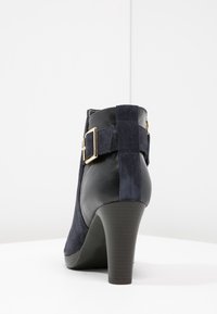 Stivaletto navy in una combinazione di camoscio e pelle. Presenta un dettaglio con fibbia dorata sul lato e un tacco affusolato. Superficie testurizzata.