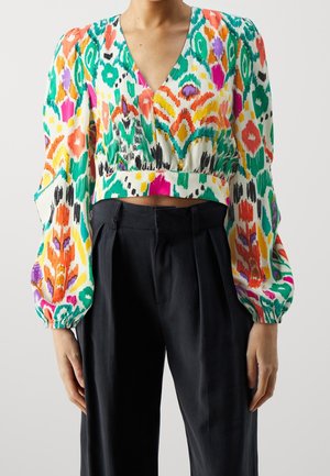 Person iført en farverig mønstret langærmet crop top med V-hals og højtaljede sorte bukser med vide ben.