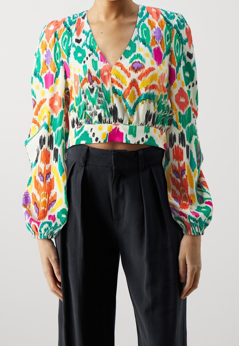 Personne portant un crop top à manches longues avec motifs colorés, un col en V et un pantalon noir taille haute à jambes larges.