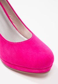 Chaussure à talon haut en daim rose vif avec bout arrondi et doublure intérieure beige sur fond blanc.