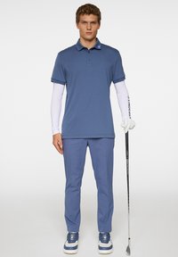 Herrgolfoutfit med en blå polo med korta ärmar, ljusblå byxor och vita sneakers. Inkluderar en golfklubba och handske.