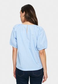 Blusa a righe blu chiaro con apertura a occhio di bue sul retro e maniche a palloncino. Il tessuto è liscio e leggero. Adatta per un look casual.