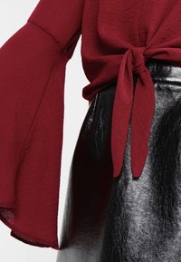 Bordeaux overdel med klokkeærmer og en samlet talje, parret med en skinnende sort faux lædernederdel med en glat tekstur.