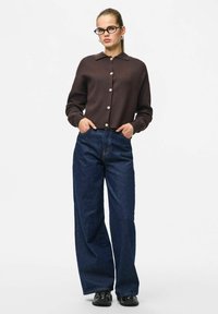 Brązowy kardigan zapinany na guziki z płaskim kołnierzem, zestawiony z granatowymi, wysokim stanem, szerokimi dżinsami i czarnymi butami. Gładka tekstura na całej powierzchni.