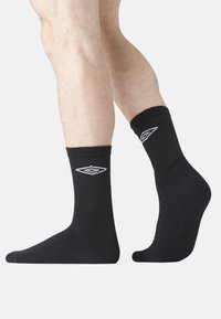 Chaussettes en coton noires à tige courte avec une texture côtelée, présentant un motif de losanges blancs sur le côté extérieur. Conçues pour le confort et la durabilité.