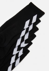 Svarta strumpor med en strukturerad stickad design och vita zigzagmönster som löper diagonalt. Topparna är uppvikta för en snug passform.
