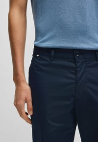 Navy blue trousers made of smooth fabric, featuring a button closure, belt loops, and a subtle metallic accent on the waistband.