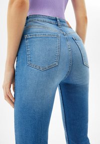 Džínové kalhoty s vysokým pasem, vyrobené z denimu, s zadními kapsami, hladkým povrchem a mírně vybledlým vzhledem.