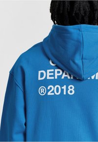 Blauwe hoodie van zachte stof met een grote witte afbeelding op de achterkant met de tekst "DEPARTEMENT" en "®2018." Inclusief capuchon met trekkoord.