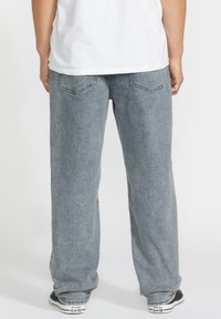 Pantalon en denim gris clair avec une coupe décontractée, doté de poches arrières doubles et de détails de couture subtils, associé à des baskets noires.