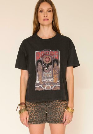 Femme portant un t-shirt noir à motif "Doors" et un short imprimé léopard, accessoirisée avec des bracelets et des bagues.