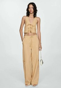 Top halter corto en color marrón con lazo delantero, combinado con pantalones amplios y sueltos en el mismo tono, que cuentan con bolsillos laterales. Tela suave, diseño casual.