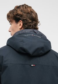 Tengerészeti kapucnis dzseki, puha tapintással, Tommy Hilfiger márkajelzéssel és egy kis háromszínű logós kiemeléssel a háton.