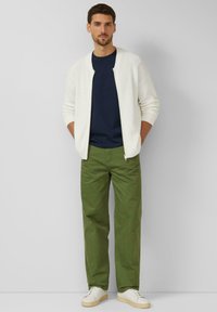 Herenoutfit bestaande uit een geribbelde witte cardigan, een marineblauw T-shirt, groene broek en witte sneakers met beige zolen. Simpel en casual ontwerp.