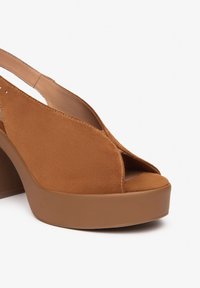 Sandales à plateforme en suède marron avec un design à bout découvert, un talon arrondi et une semelle lisse. Les détails minimalistes améliorent l'apparence globale.