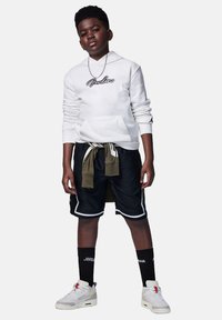 Felpa bianca con logo "Jordan", pantaloni corti neri con trim bianco e vita verde, sneakers bianche con accenti, calze nere a mezza altezza.