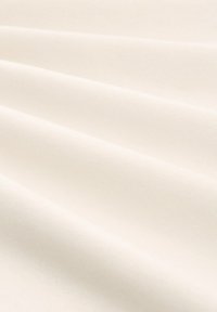 Svetlý krémový textil s jemnou, hladkou textúrou, ktorá predvádza jemné záhyby a rovnomerný vzor tkania po celom povrchu.