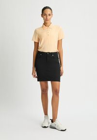 Polo shirt pesco a maniche corte con dettagli laterali, abbinato a una gonna di jeans nera. Sneakers bianche completano l'outfit.