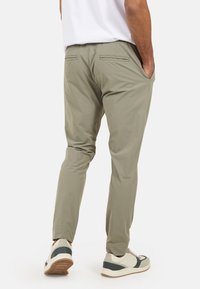 Khaki zwężane spodnie z lekkiego materiału, wyposażone w dwie tylne kieszenie i kieszenie boczne, zestawione z wielokolorowymi trampkami.