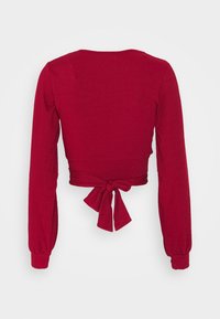 Top cropped de manga longa vermelho canelado com decote redondo e um laço nas costas. As mangas têm punhos justos.