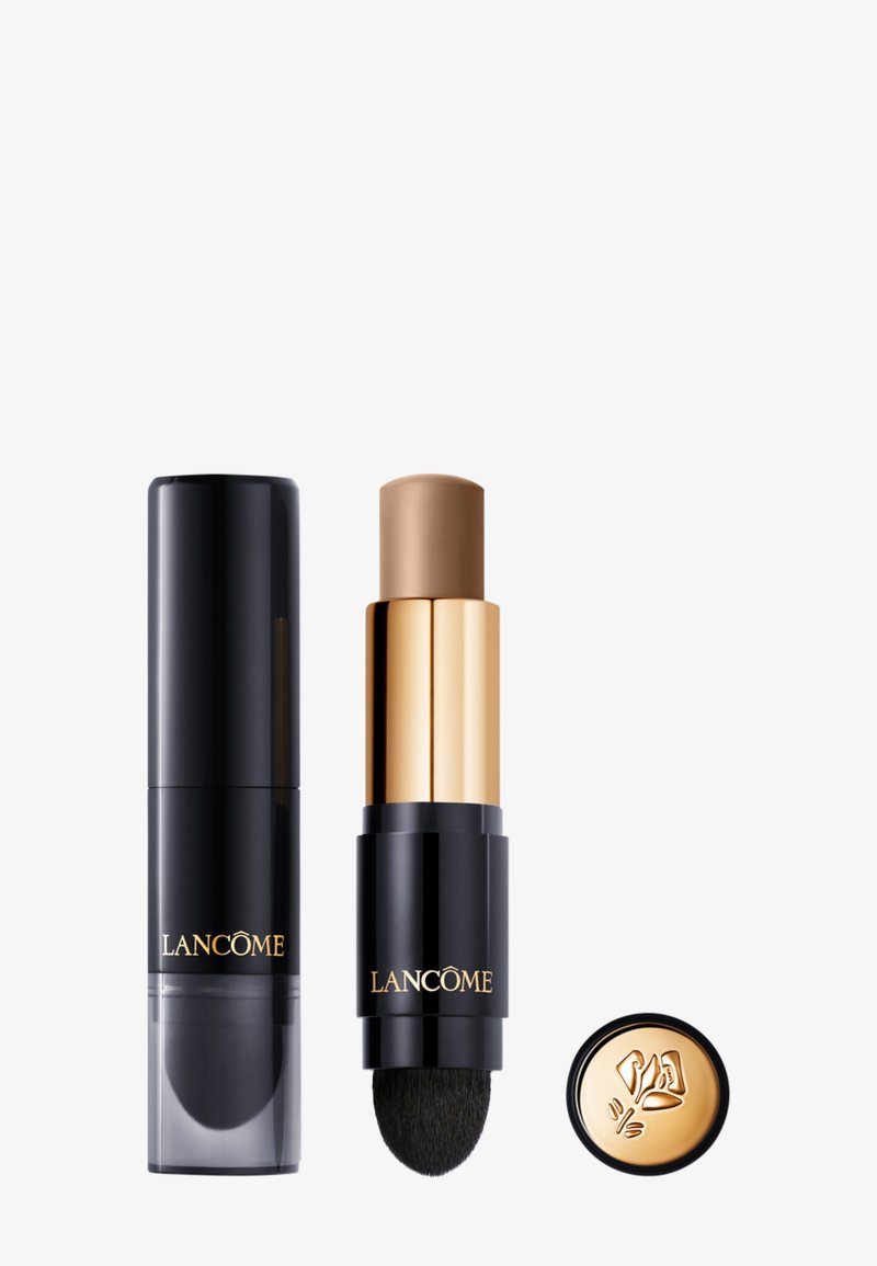 Zwarte cilindrische stick met gouden accenten en een sponsapplicator. Het product heeft een lichtbruine tint en een slank, modern ontwerp.