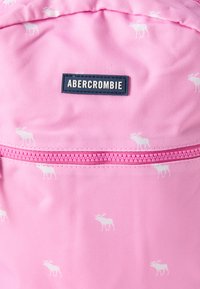Ροζ ύφασμα με μικρά λευκά μοτίβα ελαφιών, ροζ φερμουάρ και μαύρο ορθογώνιο έμπλαστρο με την επιγραφή "ABERCROMBIE".