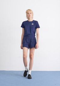 Conjunto atlético azul marinho composto por uma t-shirt de mangas curtas com um logótipo branco e calções de cintura elástica. Usado com sapatos pretos e meias brancas.