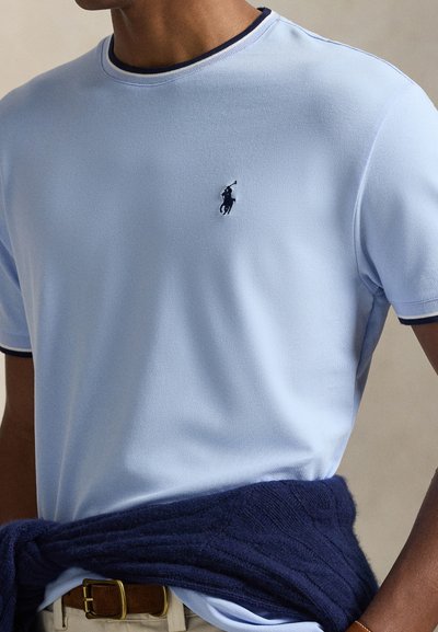 Ανοιχτό γαλάζιο πόλο με υφή υφάσματος και ναυτικούς τόνους. Διαθέτει μικρό κεντημένο λογότυπο στο στήθος και αντίθετο περίγραμμα στο λαιμό.