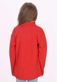 Giacca impermeabile rossa con maniche lunghe, colletto alto e design semplice. Il retro presenta un piccolo logo vicino all'orlo. Texture liscia.