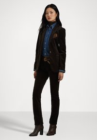 Καφέ βελούδινο σακάκι συνδυασμένο με τζιν πουκάμισο και καφέ παντελόνι. Διαθέτει μαντήλι τσέπης, ζώνη με χρυσή αλυσίδα και ψηλή μπότες.