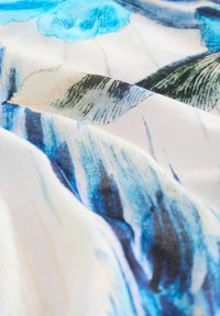 Stof met een blauw-wit bloemenpatroon, gladde textuur, met vloeiende lijnen en zachte kleurovergangen op een lichte achtergrond.
