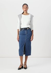 Denim keskmise pikkusega seelik ees oleva lõikega, koos valge särgi ja halli kardiganiga. Must vöö ja mustad lamedad kingad täiustavad riietust.