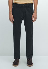 Chinos noirs à jambe droite avec une fermeture à bouton, des passants de ceinture et des poches latérales, en tissu de coton. Associés à des chaussures marron à lacets.