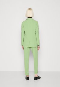 Mintgrüner Anzug mit taillierter Jacke und Hose. Textiles Material, leicht strukturierter Schnitt und schwarze Akzente am Kragen.