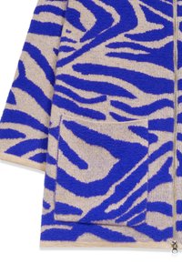 Veste en tricot beige et bleue à rayures zébrées avec poche avant et fermeture éclair argentée, présentée du milieu de la manche à l'ourlet.