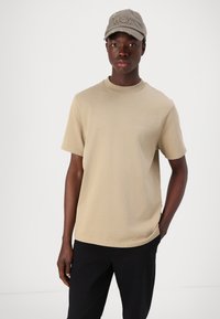 T-shirt bege de manga curta com gola redonda, feito de algodão macio. Combinado com um boné cinza com a inscrição "Won" bordada na frente.