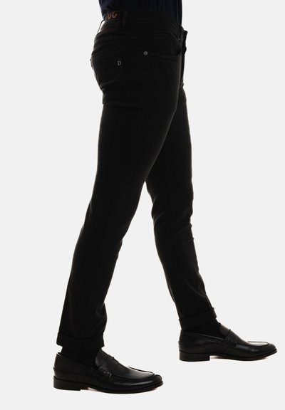 Pantaloni in denim nero con una vestibilità slim, dettagli di cucitura discreti e orlo arrotolato, abbinati a mocassini neri lucidi.