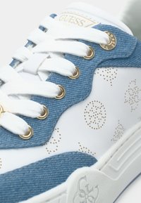 Λευκό αθλητικό παπούτσι με μπλε τζιν λεπτομέρειες, χρυσές τρύπες για κορδόνια και υφή με μικρές χρυσές κουκκίδες. Τα κορδόνια είναι λευκά.