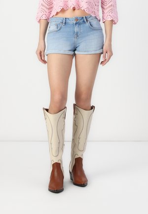 Beige western-style boots with brown leather accents and decorative stitching, featuring a tall shaft and a pointed toe design.