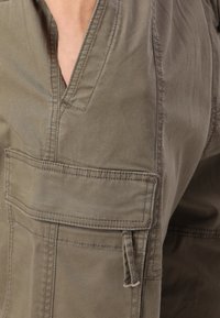 Olivgrön cargo-byxor med flera fickor, ett strukturerat bomullstyg, synliga sömdetaljer och en avslappnad passform.