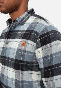 Heren geruit flanellen overhemd in blauw, zwart en wit. Voorzien van een met knopen vast te maken kraag, borstzak en een bruin logo-badge. Gestructureerde stof.